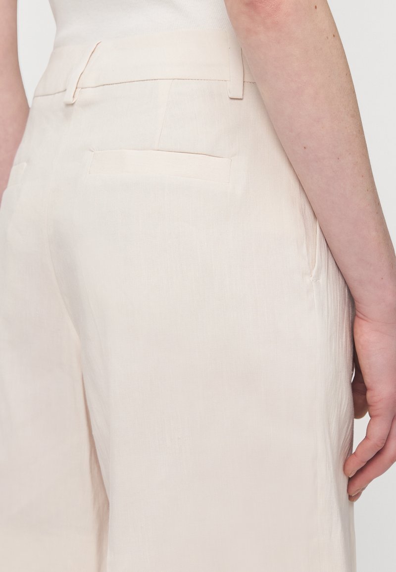 Cremefarbene Leinenhose mit glatter Textur, weitem Bein und Gesäßtaschen. Verfügt über einen dezenten Bund mit Gürtelschlaufen.