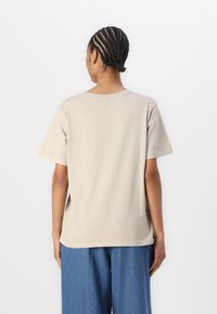 Beige bomull T-skjorte med korte ermer, rund hals og avslappet passform, sammen med blå vide bukser. Enkelt design, uten mønster.