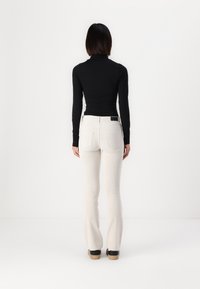 Svart långärmad polotröja som bärs med krämfärgade utsvängda byxor, med en texturerad tyg och bakfickor, i kombination med svarta skor med träklackar.