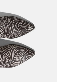 Spidse hæle med et sort og hvidt zebra-stribe mønster, lavet af glat materiale med teksturerede accenter og et slankt design.