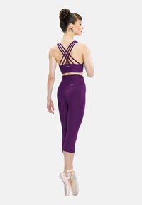 Vijoličast atletski komplet, ki vključuje športni modrček z naramnicami na hrbtu in legice do kolen. Gladka tekstura, minimalistična zasnova in oprijet kroj.