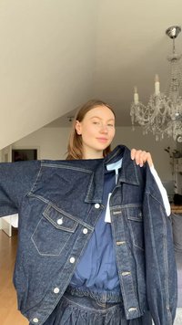 Σκούρο μπλε τζιν μπουφάν με άνετη γραμμή, διαθέτοντας κλασικές τσέπες, ασημένια κουμπιά και κίτρινες ραφές.