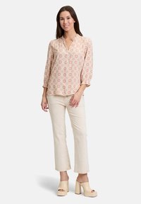 Blusa rosa chiaro con motivo e scollatura a V, maniche arricciate, abbinata a jeans dritti color crema e tacchi a piattaforma beige.