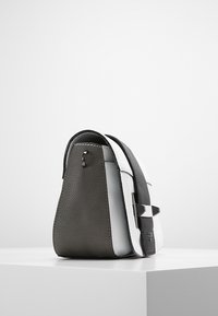 Bolsa de cuero con un frente blanco suave, parte trasera texturizada en gris oscuro y una correa negra en contraste con un acento metálico.