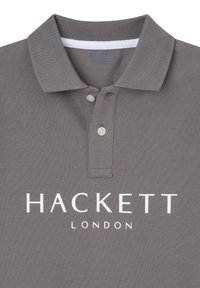 Šedé polo tričko s textúrovanou tkaninou, tri gombíky na golieri a biele logo "HACKETT LONDON" na prednej strane.