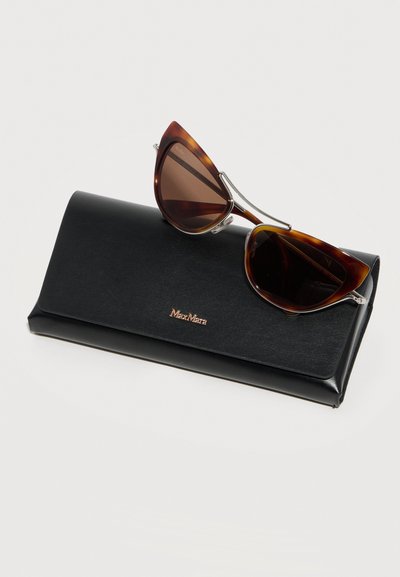 Γυαλιά ηλίου σε σχήμα γατίσιου ματιού με καφέ και μαύρο μοτίβο χελώνας, τοποθετημένα πάνω σε μαύρη δερμάτινη θήκη με την επωνυμία Max Mara, πάνω σε λευκό φόντο.