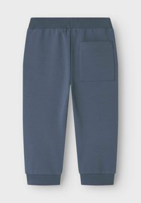 Blå bomulls-joggingbyxor med ribbad midja, smalnande benslut och en enda bakficka. Slät textur och avslappnad design.