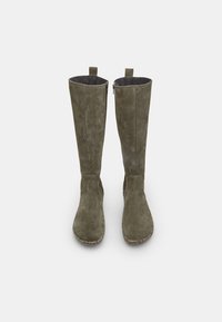 Stivali alti fino al ginocchio in suede verde oliva con texture liscia; cerniere laterali e linguette per facilitare l'indossamento. Suole in gomma con dettagli antiscivolo.
