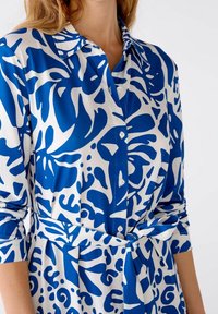 Abito button-up in un tessuto leggero caratterizzato da un audace motivo floreale astratto blu e bianco, con una cintura da annodare in vita e maniche arrotolabili.
