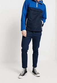 Navy and blue color-blocked pullover jacket with half-zip, front pocket, paired with dark blue pants and black high-top sneakers.