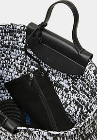 Sac fourre-tout en paille tissée noir et blanc avec une poignée en cuir noir et une poche zippée, présentant une finition texturée et un design fonctionnel.