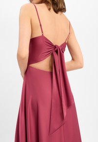 Magenta satijnen jurk met dunne bandjes, heeft een geknoopte cut-out achterkant en een vloeiende rok, die een soepele textuur en een elegante uitstraling toont.