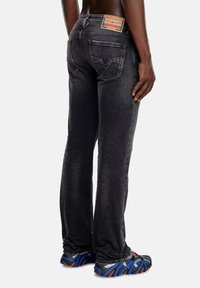 Black denim jeans with a straight cut, featuring two back pockets and a label on the waistband. Worn with blue and gray athletic shoes.