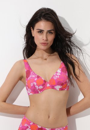 Donna con capelli lunghi e scuri che indossa un top bikini con motivo floreale rosa e arancione su sfondo bianco.