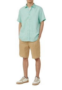 Lichtblauw kortom mouwshirt met knopen, tan shorts en witte sneakers met lichte accenten. De stof lijkt zacht en lichtgewicht.