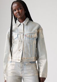 Metallic silver denimjacka med två bröstfickor, knäppning fram och krage. Har kontrasterande sömmar och en kort design.