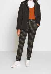 Svart vadderad jacka, orange ribbad tröja och byxor i svart-vitt rutmönster med vita sneakers. Slätt tyg, figursydd design och kontrasterande mönster.