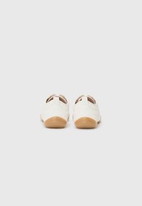 Chaussures en cuir blanc avec une texture lisse, une forme arrondie et des semelles en caoutchouc. Elles présentent un petit talon et des coutures discrètes sur les côtés.
