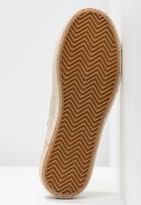 Suela de goma marrón con un patrón en zigzag, parte superior de yute texturizado y bordes redondeados. Diseño limpio, con un minimalismo en los detalles, que resalta un aspecto de fibra natural.