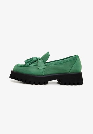 Zielone zamszowe loafersy z detalem w postaci kokardy i frędzlami, z grubą czarną gumową podeszwą o ząbkowanej krawędzi.
