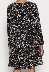 Schwarzes Kleid mit langen Ärmeln, einem runden Ausschnitt und einem gestuften Saum. Es hat ein verstreutes weißes Blumenmuster auf einem strukturierten Stoff.