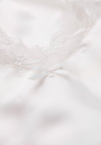 Satin nattlinne med en dekorativ spetskrage och en liten vit rosett i mitten. Färgen är mjuk vit med en slät textur.