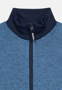 Μπλε φλις μπουφάν με ψηλό γιακά και εμπρός φερμουάρ, με υφή υφάσματος και αντίθετες ναυτικές λεπτομέρειες κατά μήκος του φερμουάρ.