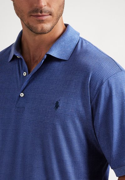 Άνδρας που φοράει μπλε καρό πόλο πουκάμισο με γιακά και δύο κουμπιά, εμφανίζοντας το στήθος και την περιοχή των ώμων.