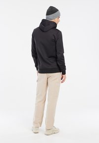 Zwarte hoodie met een trekkoord en geribbelde manchetten, gecombineerd met beige cargobroek. Een grijze beanie maakt de outfit compleet. Textuurstof en casual pasvorm.