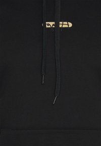 Sudadera con capucha negra con un logo bordado en oro, cordones negros con terminales metálicos y un bolsillo canguro en la parte delantera.