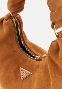 Bruine suede handtas met een gouden rits, driehoekig logo-accent en een zachte, gestructureerde afwerking met een geknoopt hengsel.