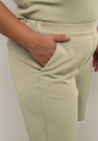 Pantalones de color verde claro hechos de tela elástica, con una cintura de tamaño medio y bolsillos laterales. La textura parece suave y lisa.