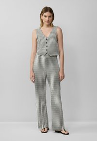 Gestreiftes ärmelloses Oberteil mit V-Ausschnitt und Knopfdetails, kombiniert mit weit geschnittenen Hosen. Schwarz-weiße Farben, glatte Textur, lässiges Design.