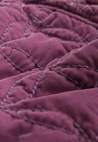 Nahaufnahme eines weichen, violetten Steppstoffs mit detaillierter, geschwungener Naht und strukturierten, gepolsterten Bereichen.