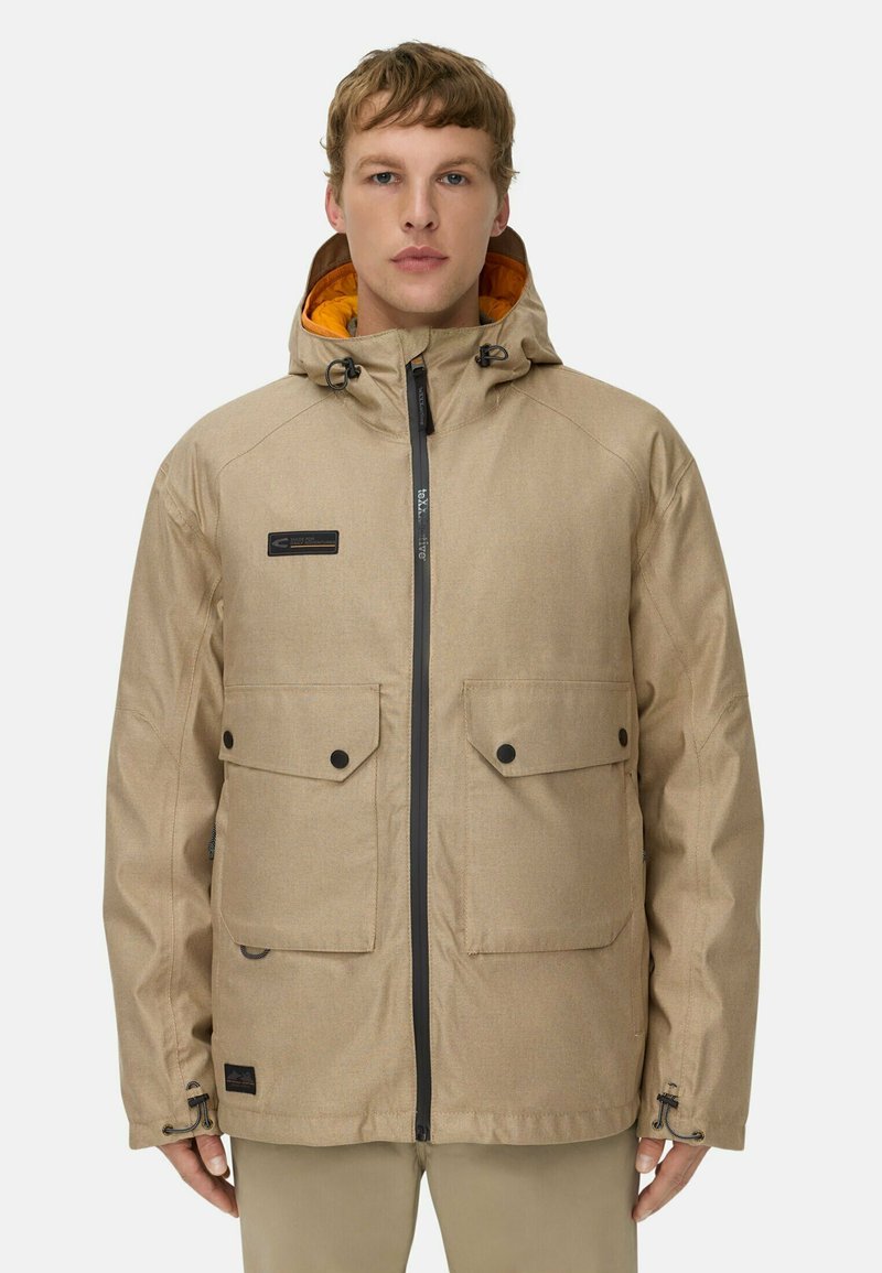 Beige vandtæt jakke med lynlås foran, justerbar hætte, to store frontlommer og kontrasterende orange for. Blød tekstur.