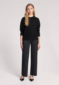 Czarny sweter dzianinowy z prążkowanym dołem, zestawiony z czarnymi spodniami w paski i czarnymi, spiczastymi butami. Gładki materiał o luźnym kroju.