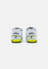 Scarpe da ginnastica bianche con accenti neri, suola gialla e tomaia in rete traspirante caratterizzata da un design testurizzato e il marchio 'Joma' sul tallone.