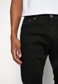 Černé džíny z denimu se slim fit, mají pět kapes, kovové detaily a decentní švy. Tkanina má hladkou texturu.