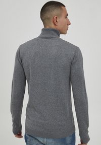 Grå turtleneck sweater med lange ærmer, lavet af struktureret strikstof, med ribbede manchetter og kant. Bæres med blå jeans.