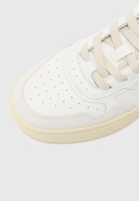 Sneaker in pelle bianca con lacci beige, punta perforata e dettagli in suede marrone. Caratterizzato da suola in gomma con dettagli testurizzati.