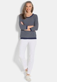 Maglione a righe blu e bianche con maniche lunghe e polsini, abbinato a pantaloni bianchi e sneakers bianche. Texture a maglia liscia.