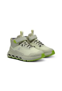 Chaussures gris clair avec une finition imperméable, présentant une surface texturée, des accents verts et une semelle rembourrée avec des trous de drainage.