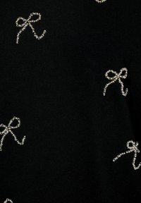 Tejido negro con pequeños adornios en forma de lazo de cuentas plateadas dispersos en la superficie.