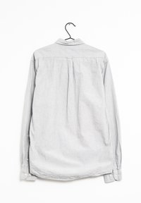 Košile s dlouhým rukávem ve světlém šedém materiálu s texturovaným povrchem, s manžetami na jeden knoflík, zadními sklady a klasickým límečkem, visící na černém háčku.