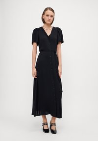 Vestito maxi nero con colletto a button-down, maniche a palloncino corte, vita aderente e gonna fluida. Tessuto liscia con una leggera lucentezza.