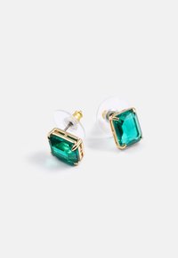 Pendientes de aro cuadrados de esmeralda verde con tachuelas doradas y respaldos de plástico transparente sobre una superficie blanca.