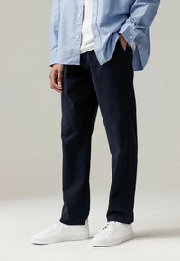 Pantaloni bleumarin cu o croială dreaptă, realizați dintr-un material rezistent. Purtați cu o cămașă bleu deschis și adidași albi. Prezintă buzunare frontale.