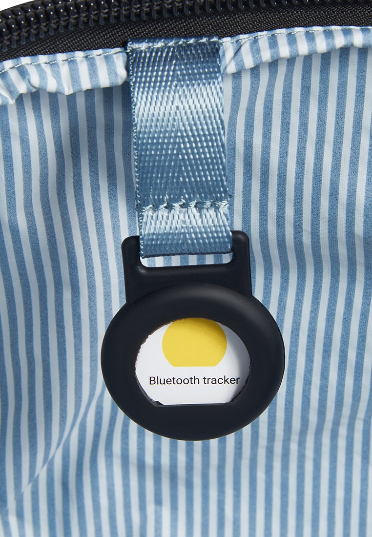 Blau-weißer gestreifter Stoff mit einem schwarzen Reißverschluss. Verfügt über einen runden schwarzen Halter für ein gelbes Bluetooth-Tracker-Etikett.