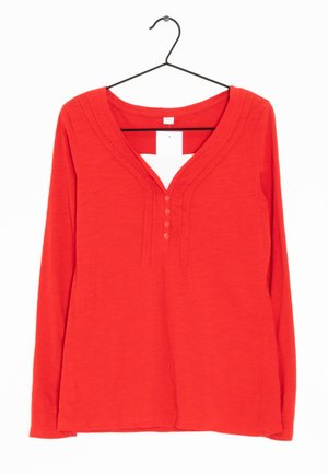 Rotes Langarmoberteil mit tiefem V-Ausschnitt, das drei Knöpfe und dezente Details entlang des Ausschnitts aufweist. Hergestellt aus weichem, strukturiertem Stoff.