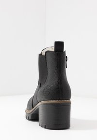 Botte noire à la cheville avec une finition en cuir texturé, un talon épais, une fermeture éclair sur le côté et une doublure blanche douce. Détail du logo sur le côté extérieur.